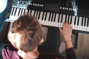 Güneşli bir odada dijital klavye çalan bir insanın genel görünümü, yumuşak doğal ışık ve rahat bir atmosferle bir odak ve yaratıcılık anını vurguluyor. Müzik hayatı.