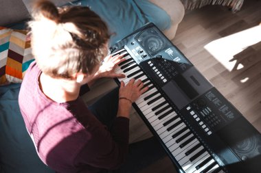 Güneşli bir odada dijital klavye çalan bir insanın genel görünümü, yumuşak doğal ışık ve rahat bir atmosferle bir odak ve yaratıcılık anını vurguluyor. Müzik hayatı.