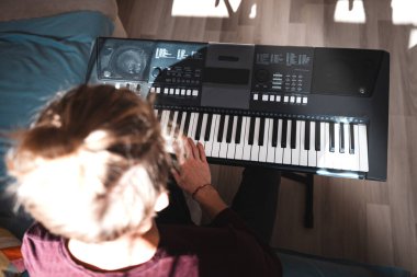 Güneşli bir odada dijital klavye çalan bir insanın genel görünümü, yumuşak doğal ışık ve rahat bir atmosferle bir odak ve yaratıcılık anını vurguluyor. Müzik hayatı.