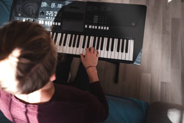 Güneşli bir odada dijital klavye çalan bir insanın genel görünümü, yumuşak doğal ışık ve rahat bir atmosferle bir odak ve yaratıcılık anını vurguluyor. Müzik hayatı.