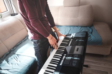 Konforlu mobilyalar ve yumuşak dokularla çevrili aydınlık bir oturma odasında dijital bir klavye çalan müzisyen, dinamik müzik yaratıcılığı sergiliyor..