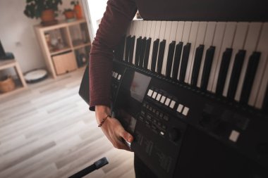 Modern bir oturma odasında elinde dijital bir klavye tutan kişi, bir anlık müzikal geçiş sergiliyor, yumuşak doğal ışık, minimalist iç dekorun altını çiziyor.