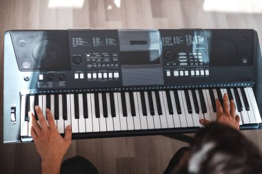 Rahat bir ev ortamında dijital klavye çalan bir adam, koltuğa oturmuş, doğal ışık içeri akıyor, huzurlu ve odaklanmış bir müzik anı yakalıyor..