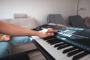 Close-up of a digital keyboard with a hand playing a melody, illuminated by soft natural light. The detailed controls and keys evoke creativity and musical exploration. clipart