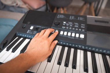 Yumuşak doğal ışıkla aydınlatılmış, melodi çalan bir eli olan dijital bir klavyenin yakın çekimi. Detaylı kontroller ve anahtarlar yaratıcılığı ve müzikal keşifleri çağrıştırıyor.