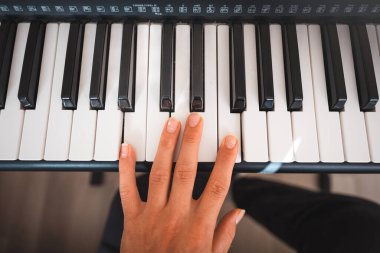 Yumuşak doğal ışıkla aydınlatılmış, melodi çalan bir eli olan dijital bir klavyenin yakın çekimi. Detaylı kontroller ve anahtarlar yaratıcılığı ve müzikal keşifleri çağrıştırıyor.
