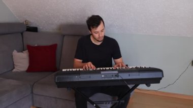 Odaklanmış müzisyen ince melodileri ve rahat bir oturma odasında elektronik bir klavye çalıyor. Sahne yaratıcılığı, kararlılığı ve müziğe olan tutkuyu vurguluyor.