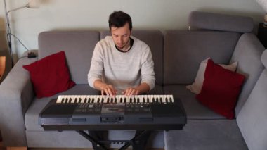 Odaklanmış müzisyen ince melodileri ve rahat bir oturma odasında elektronik bir klavye çalıyor. Sahne yaratıcılığı, kararlılığı ve müziğe olan tutkuyu vurguluyor.