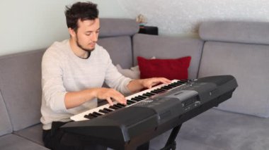 Odaklanmış müzisyen ince melodileri ve rahat bir oturma odasında elektronik bir klavye çalıyor. Sahne yaratıcılığı, kararlılığı ve müziğe olan tutkuyu vurguluyor.