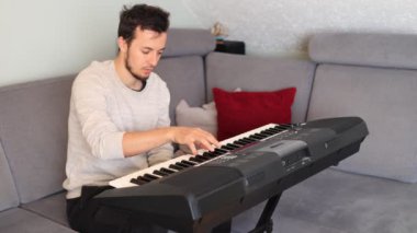Odaklanmış müzisyen ince melodileri ve rahat bir oturma odasında elektronik bir klavye çalıyor. Sahne yaratıcılığı, kararlılığı ve müziğe olan tutkuyu vurguluyor.