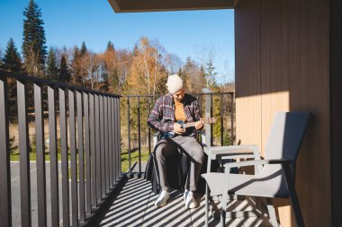Genç müzisyen, ukulele çalmaya dalmış güneşli bir balkonda oturuyor. Etrafı sonbahar ağaçlarıyla çevrili, dışarıda huzurlu bir anın tadını çıkarıyor, düşüncelerinde ve müziğinde kayboluyor.