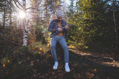 Genç adam güneşli bir ormanda ağaç kütüğünde oturur ve ukulele çalar. Sonbahar renkleri ve ağaçların arasından süzülen yumuşak güneş ışığıyla çevrelenmiş doğa ve müzikle barışçıl bir bağ kuruyor..