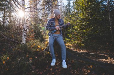 Genç adam güneşli bir ormanda ağaç kütüğünde oturur ve ukulele çalar. Sonbahar renkleri ve ağaçların arasından süzülen yumuşak güneş ışığıyla çevrelenmiş doğa ve müzikle barışçıl bir bağ kuruyor..