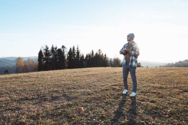 Müzisyen, güneşli bir sonbahar gününde elinde ukulele ile açık bir alanda duruyor. Tepeler ve ağaçlarla çevrili sakin sahne özgürlüğü, yaratıcılığı ve doğayla olan bağlantıyı yansıtıyor..