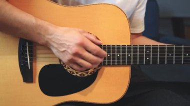 Müzisyenlerin elleri nazikçe akustik gitar tellerini tıngırdatıyor, evin içindeki sıcak ışık parlayan ahşabı yansıtırken karmaşık hareketleri ve hassasiyeti yakalıyor.
