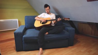 Müzisyen sıcak bir oturma odasında sıcak bir kanepede oturup akustik gitar tıngırdatıyor. Video, onların rahat duruşlarını ve müziğin rahatlatıcı tonlarını yakalıyor.