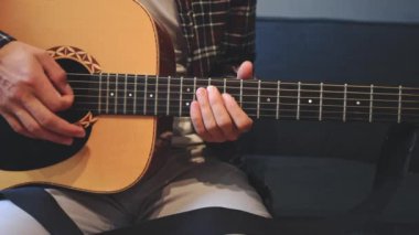 Müzisyenlerin elleri nazikçe akustik gitar tellerini tıngırdatıyor, evin içindeki sıcak ışık parlayan ahşabı yansıtırken karmaşık hareketleri ve hassasiyeti yakalıyor.