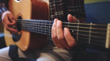 Müzisyenlerin elleri nazikçe akustik gitar tellerini tıngırdatıyor, evin içindeki sıcak ışık parlayan ahşabı yansıtırken karmaşık hareketleri ve hassasiyeti yakalıyor.