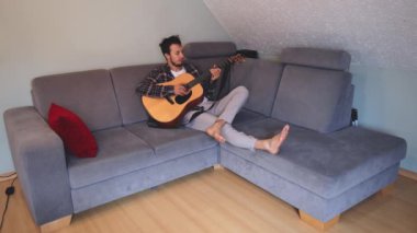 Müzisyen sıcak bir oturma odasında sıcak bir kanepede oturup akustik gitar tıngırdatıyor. Video, onların rahat duruşlarını ve müziğin rahatlatıcı tonlarını yakalıyor.