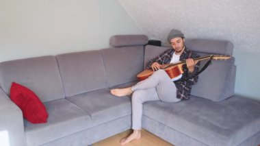 Müzisyen sıcak bir oturma odasında sıcak bir kanepede oturup akustik gitar tıngırdatıyor. Video, onların rahat duruşlarını ve müziğin rahatlatıcı tonlarını yakalıyor.