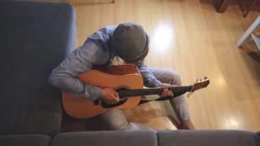 Müzisyen sıcak bir oturma odasında sıcak bir kanepede oturup akustik gitar tıngırdatıyor. Video, onların rahat duruşlarını ve müziğin rahatlatıcı tonlarını yakalıyor.