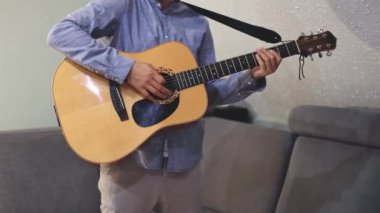 Müzisyenlerin elleri nazikçe akustik gitar tellerini tıngırdatıyor, evin içindeki sıcak ışık parlayan ahşabı yansıtırken karmaşık hareketleri ve hassasiyeti yakalıyor.
