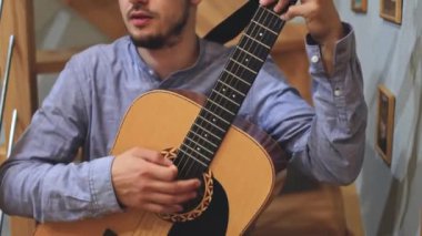 Müzisyenlerin elleri nazikçe akustik gitar tellerini tıngırdatıyor, evin içindeki sıcak ışık parlayan ahşabı yansıtırken karmaşık hareketleri ve hassasiyeti yakalıyor.