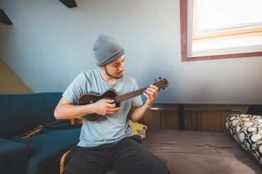 Gülümseyen bir müzisyen rahat bir yatakta oturup siyah bir ukulele tıngırdatıyor. Ukulele çalmanın ve kendini yaratıcı ruha daldırmanın tadını çıkarıyorum..