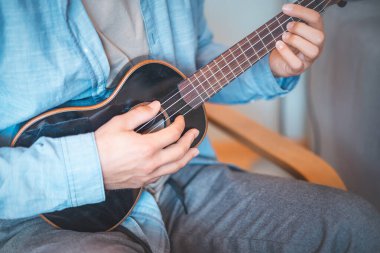 Yakından bakınca, parlak siyah bir ukulelenin tellerini koparan bir adamın parmaklarını yakalıyor. Müzik yapıyorum. Bir enstrüman çalmanın zevki.