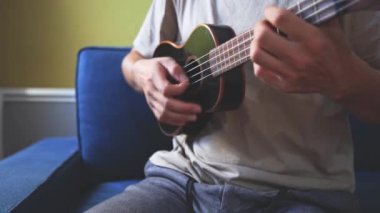 Gelişmekte olan bir müzisyenin siyah ukulele çalmayı öğrenip, müzik yeteneklerini derinleştirmesinin detaylı görüntüleri. Evlerinin konforunda telleri tıngırdatarak