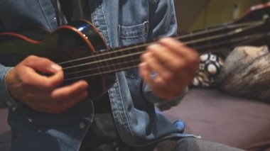 Gelişmekte olan bir müzisyenin siyah ukulele çalmayı öğrenip, müzik yeteneklerini derinleştirmesinin detaylı görüntüleri. Evlerinin konforunda telleri tıngırdatarak