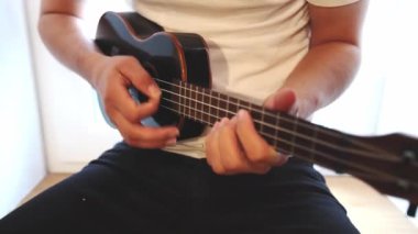 Gelişmekte olan bir müzisyenin siyah ukulele çalmayı öğrenip, müzik yeteneklerini derinleştirmesinin detaylı görüntüleri. Evlerinin konforunda telleri tıngırdatarak