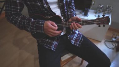 Gelişmekte olan bir müzisyenin siyah ukulele çalmayı öğrenip, müzik yeteneklerini derinleştirmesinin detaylı görüntüleri. Evlerinin konforunda telleri tıngırdatarak