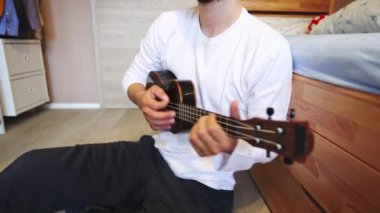 Gelişmekte olan bir müzisyenin siyah ukulele çalmayı öğrenip, müzik yeteneklerini derinleştirmesinin detaylı görüntüleri. Evlerinin konforunda telleri tıngırdatarak