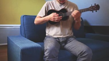 Gelişmekte olan bir müzisyenin siyah ukulele çalmayı öğrenip, müzik yeteneklerini derinleştirmesinin detaylı görüntüleri. Evlerinin konforunda telleri tıngırdatarak