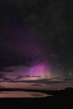 Snaefellsnes yarımadası üzerinde Aurora borealis, Batı İzlanda, canlı mor ve pembe renkler, yıldızlı gece gökyüzü, durgun su yansıması, nefes kesici doğa harikası.