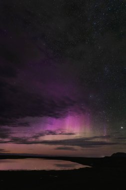 Snaefellsnes yarımadası üzerinde Aurora borealis, Batı İzlanda, canlı mor ve pembe renkler, yıldızlı gece gökyüzü, durgun su yansıması, nefes kesici doğa harikası.