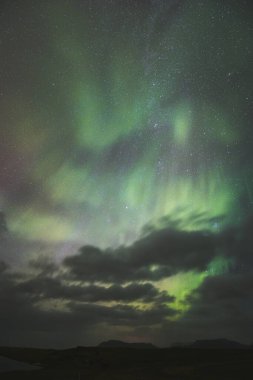 Kuzey Avrupa 'da dramatik bir gece gökyüzü. Yeşil aurora borealis pembe ve mor tonlarla harmanlanırken parlak yıldızlar içinden parlar. Snaefellsnes Yarımadası, Batı İzlanda. Dikey fotoğraf.