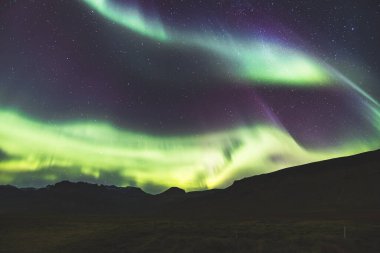 Kuzey ışıkları, Aurora borealis, Batı İzlanda 'daki Snaefellsnes yarımadasındaki kayalık volkanik dağların üzerinde çeşitli renklerde gece gökyüzü boyunca uzanır. Bir gece masalı.
