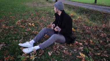 Tutkulu 26 yaşındaki müzisyen günbatımında gitar çalarak açık havada eğleniyor. Doğada olmak. Modern halk tarzında doğa ve müziğe duyulan sevginin bir karışımı. 4k video