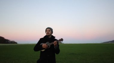 Tutkulu 26 yaşındaki müzisyen günbatımında gitar çalarak açık havada eğleniyor. Doğada olmak. Modern halk tarzında doğa ve müziğe duyulan sevginin bir karışımı. 4k video