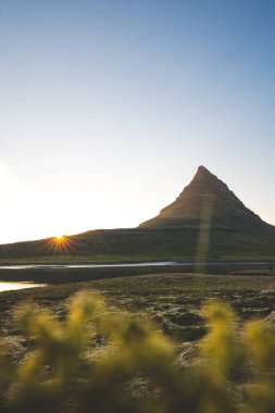 Güneş batarken İzlanda 'daki Snaefellsnes yarımadasında Kirkjufell Dağı. İkonik zirve, akşam gökyüzünün canlı renkleriyle çevrili sakin sulara yansıyor..