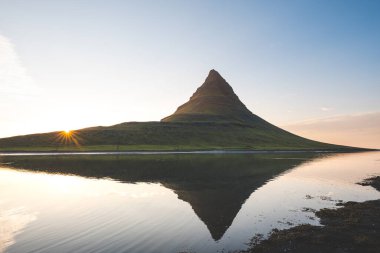 Güneş batarken İzlanda 'daki Snaefellsnes yarımadasında Kirkjufell Dağı. İkonik zirve, akşam gökyüzünün canlı renkleriyle çevrili sakin sulara yansıyor..