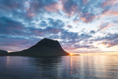 Güneş batarken İzlanda 'daki Snaefellsnes yarımadasında Kirkjufell Dağı. İkonik zirve, akşam gökyüzünün canlı renkleriyle çevrili sakin sulara yansıyor..