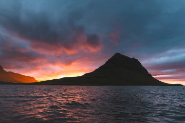 Güneş batarken İzlanda 'daki Snaefellsnes yarımadasında Kirkjufell Dağı. İkonik zirve, akşam gökyüzünün canlı renkleriyle çevrili sakin sulara yansıyor..