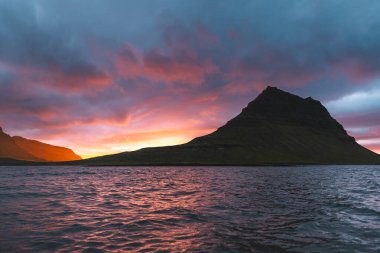 Güneş batarken İzlanda 'daki Snaefellsnes yarımadasında Kirkjufell Dağı. İkonik zirve, akşam gökyüzünün canlı renkleriyle çevrili sakin sulara yansıyor..