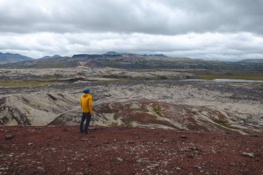 Sarı ceketli bir adam İzlanda 'daki Snafellsnes Yarımadası' ndaki kırmızı lav tarlasının tepesinde duruyor. Uçsuz bucaksız engebeli bir araziye bakıyor..