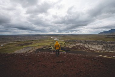 Sarı ceketli bir adam İzlanda 'daki Snafellsnes Yarımadası' ndaki kırmızı lav tarlasının tepesinde duruyor. Uçsuz bucaksız engebeli bir araziye bakıyor..