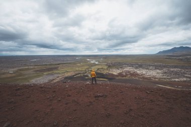 Sarı ceketli bir adam İzlanda 'daki Snafellsnes Yarımadası' ndaki kırmızı lav tarlasının tepesinde duruyor. Uçsuz bucaksız engebeli bir araziye bakıyor..