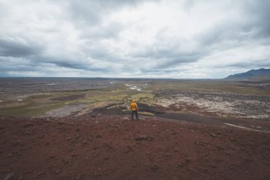Sarı ceketli bir adam İzlanda 'daki Snafellsnes Yarımadası' ndaki kırmızı lav tarlasının tepesinde duruyor. Uçsuz bucaksız engebeli bir araziye bakıyor..